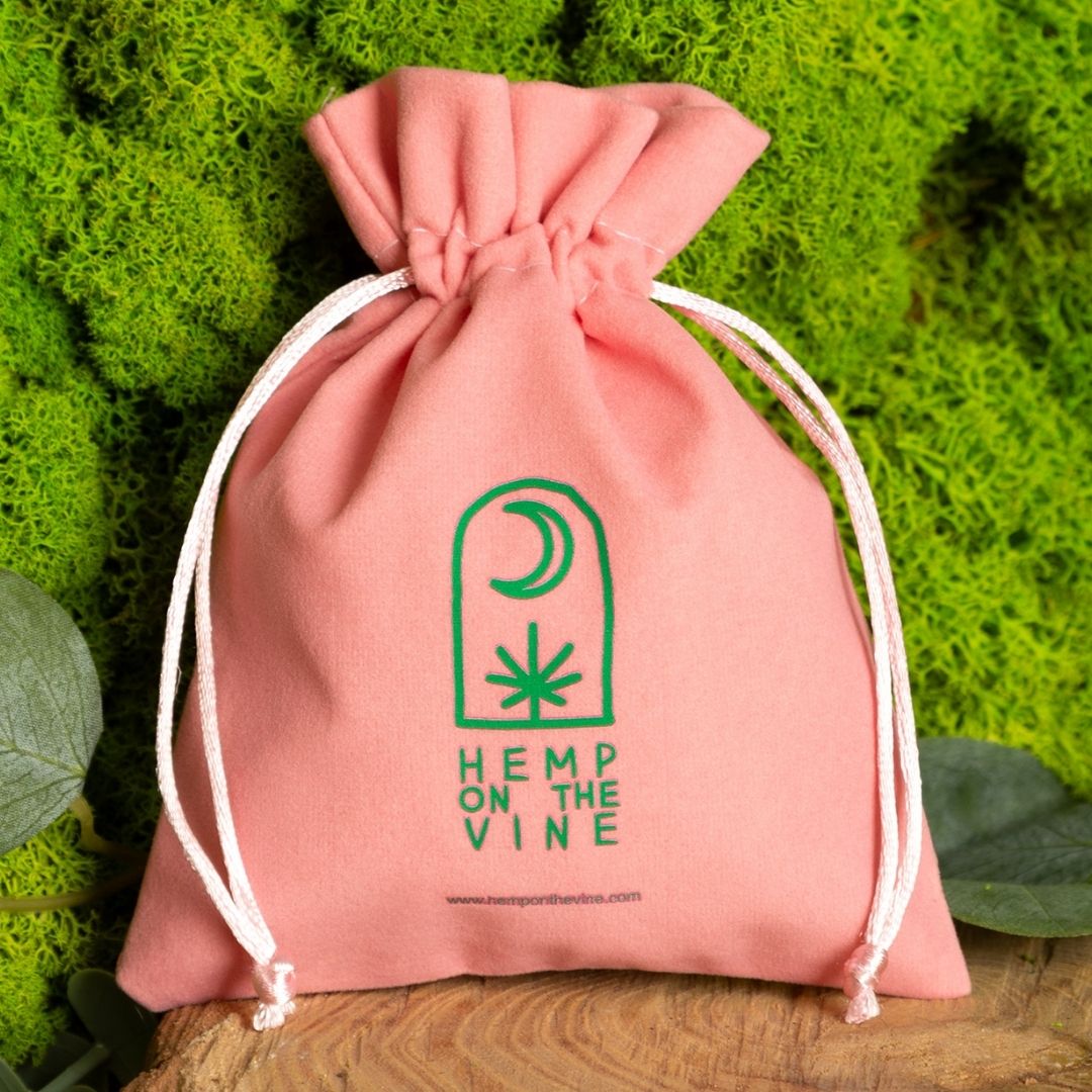 Saco de terciopelo rosa con motivo vegetal verde y logo.