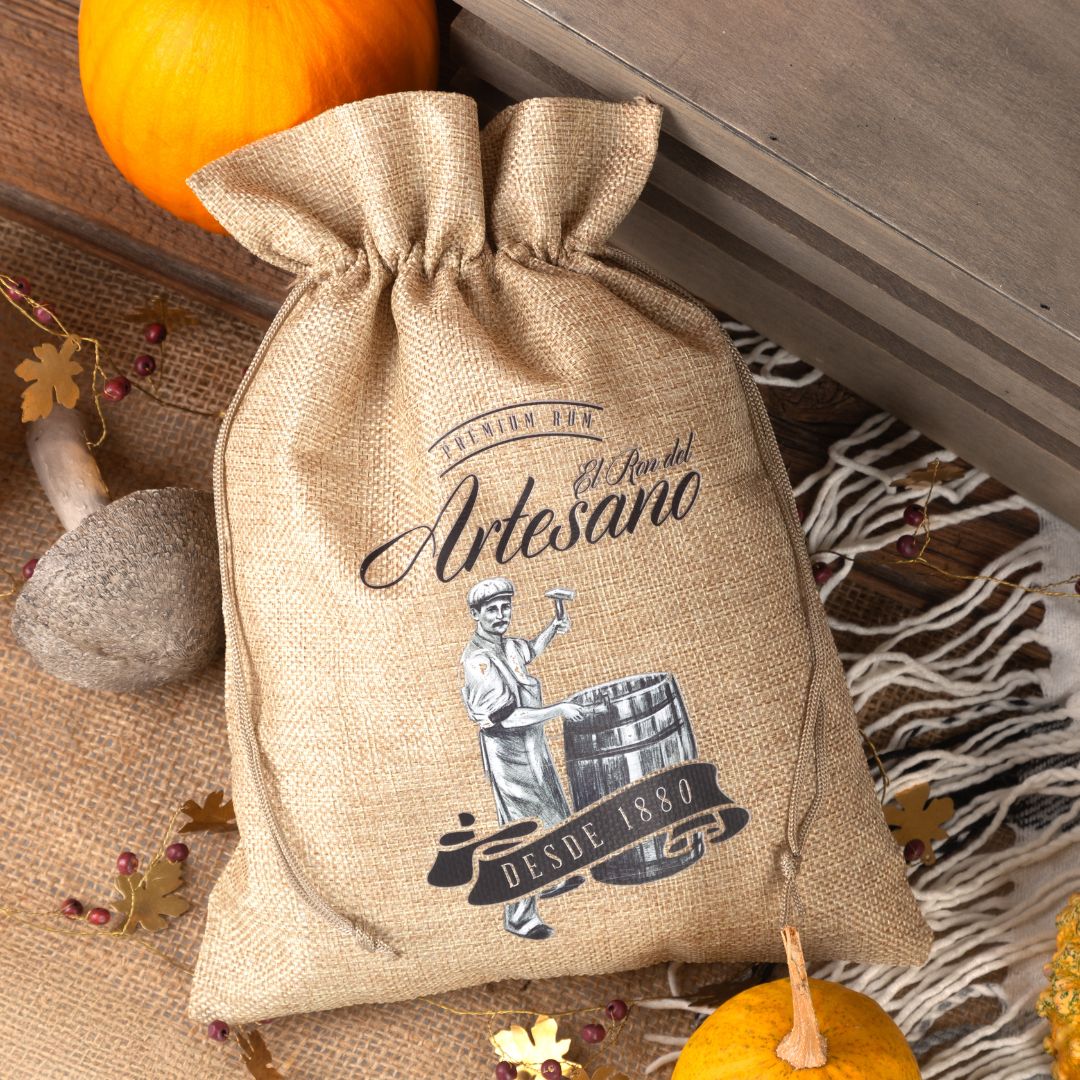 Bolsa de yute con estampado negro "Artesano", frente a una decoración otoñal.