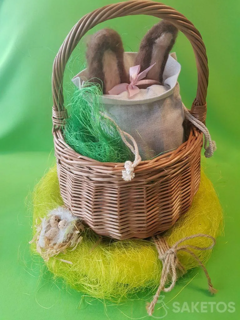 Cesta con una bolsa de lino de la que sobresalen las orejas de un conejo de lana peinada.