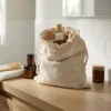 Bolsa de lino en una estantería de baño con cosméticos y accesorios de madera en un interior luminoso